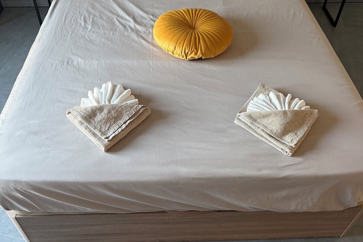 A neatly made bed with a headboard, two bedside tables, and a single yellow accent pillow.