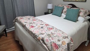 Un llit ben arreglat amb roba de llit floral, una làmpada de nit i un quadre floral a la paret.