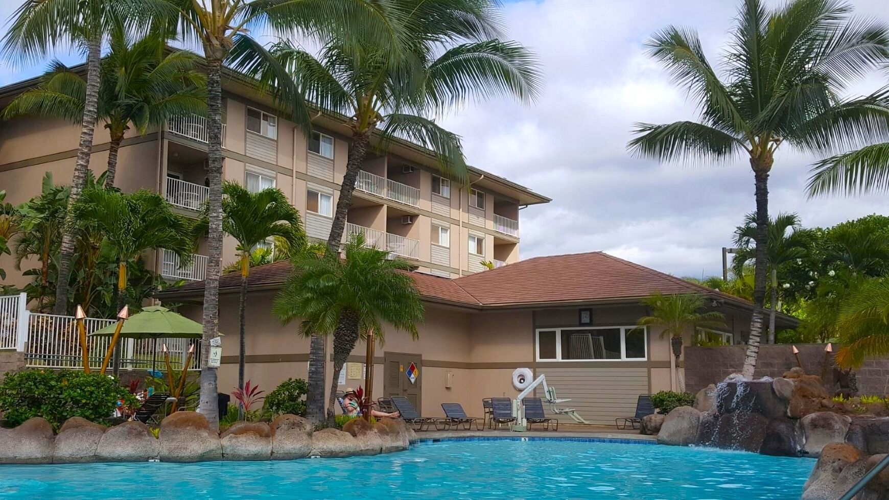 A hotel with a swimming pool, palm trees, and a multi-story building with balconies.