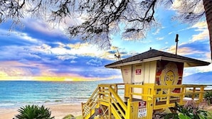 Une tour de surveillance avec un panneau indiquant « DÉFENSE D’ENTRER » se dresse sur une plage, offrant une vue sur l’océan et un ciel au coucher du soleil.