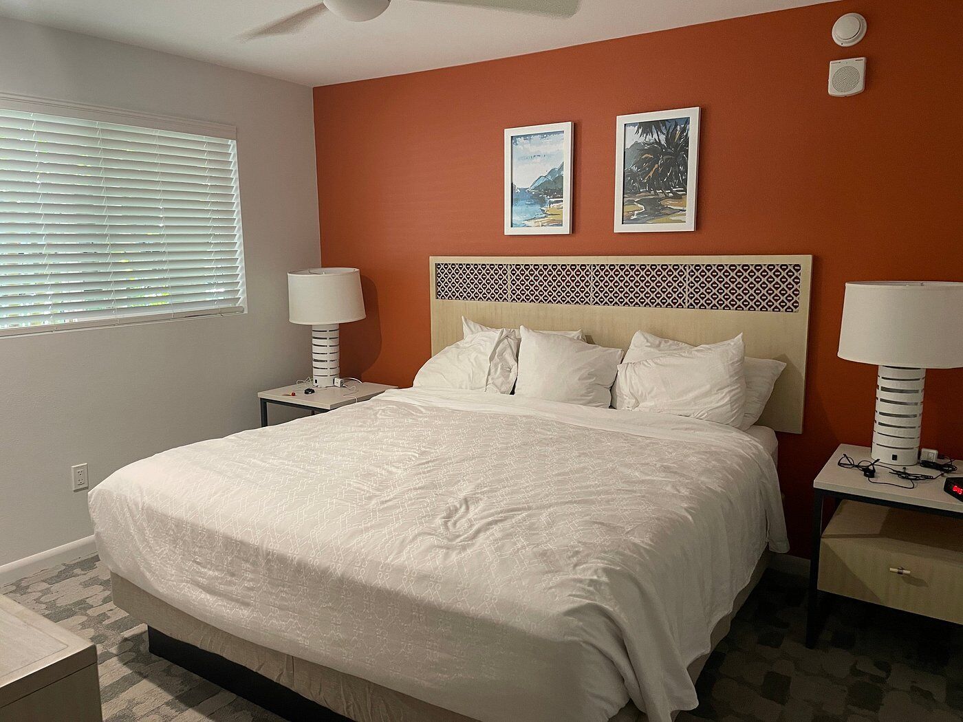 A neatly arranged bedroom with a large bed, two bedside tables with lamps, a patterned headboard, and two framed pictures on the wall.