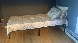 A single bed with a floral bedspread in a room with wooden flooring and dark walls.