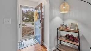 Un ingresso moderno con una porta blu, una lampada intrecciata e un cartello di benvenuto.