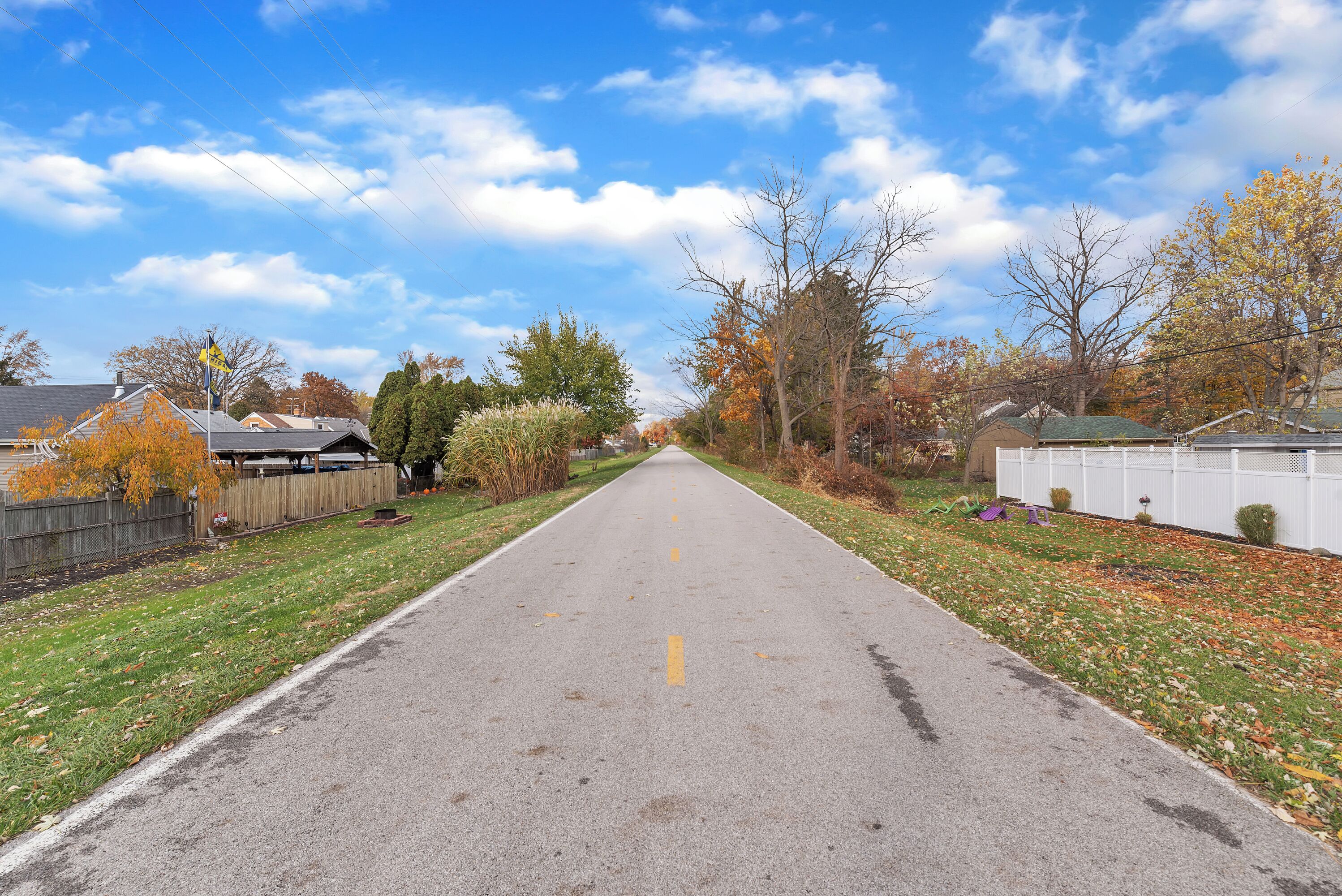 Eine gerade Straße, gesäumt von Häusern und Bäumen mit Herbstlaub.