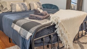Un letto rifatto con cura, una coperta a quadretti blu e bianchi, un plaid bianco piegato e una testiera blu scuro.