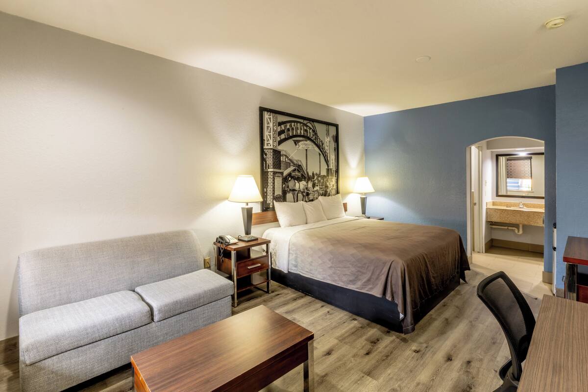 A hotel room with a bed, a sofa, a desk, a lamp, and a painting on the wall.