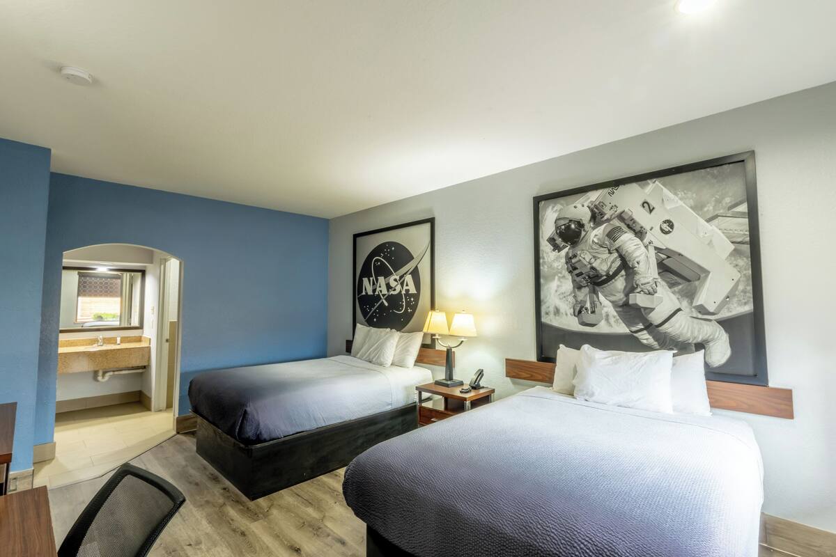 A hotel room with two beds, a bathroom, a desk, and a window.