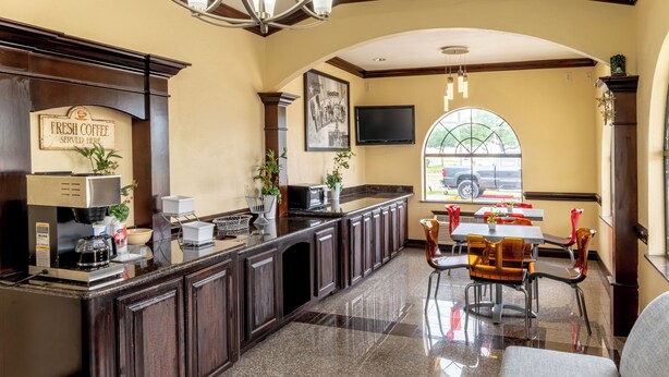 A kitchen with a coffee station, a dining area with chairs, a chandelier, and a large window. - Azul Inn Houston Hobby Airport (Houston)