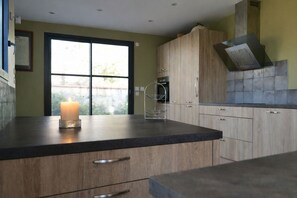 A modern kitchen with wooden cabinets, a black countertop, and a lit candle. - Large house with enclosed garden for 8 people (Olonne-sur-Mer)