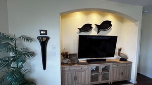 Una sala de estar con un televisor de pantalla plana montado en un mueble de madera, una lámpara de pared y una planta en maceta.