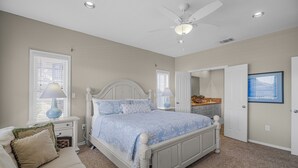Un dormitorio con cama, mesitas de noche, ventilador de techo y puerta que da al baño.