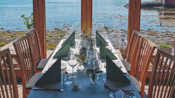 Mesa dispuesta para comer con vista a un lago y montañas.