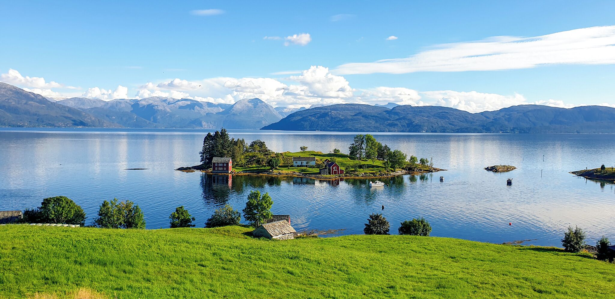 Escena serena junto al lago con una pequeña isla que presenta edificios tradicionales, rodeada de exuberante vegetación y montañas distantes.