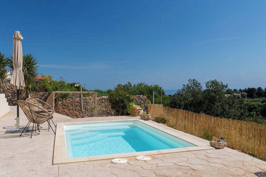 Una piscina con bordo in pietra, sedie in vimini e vista sul mare.