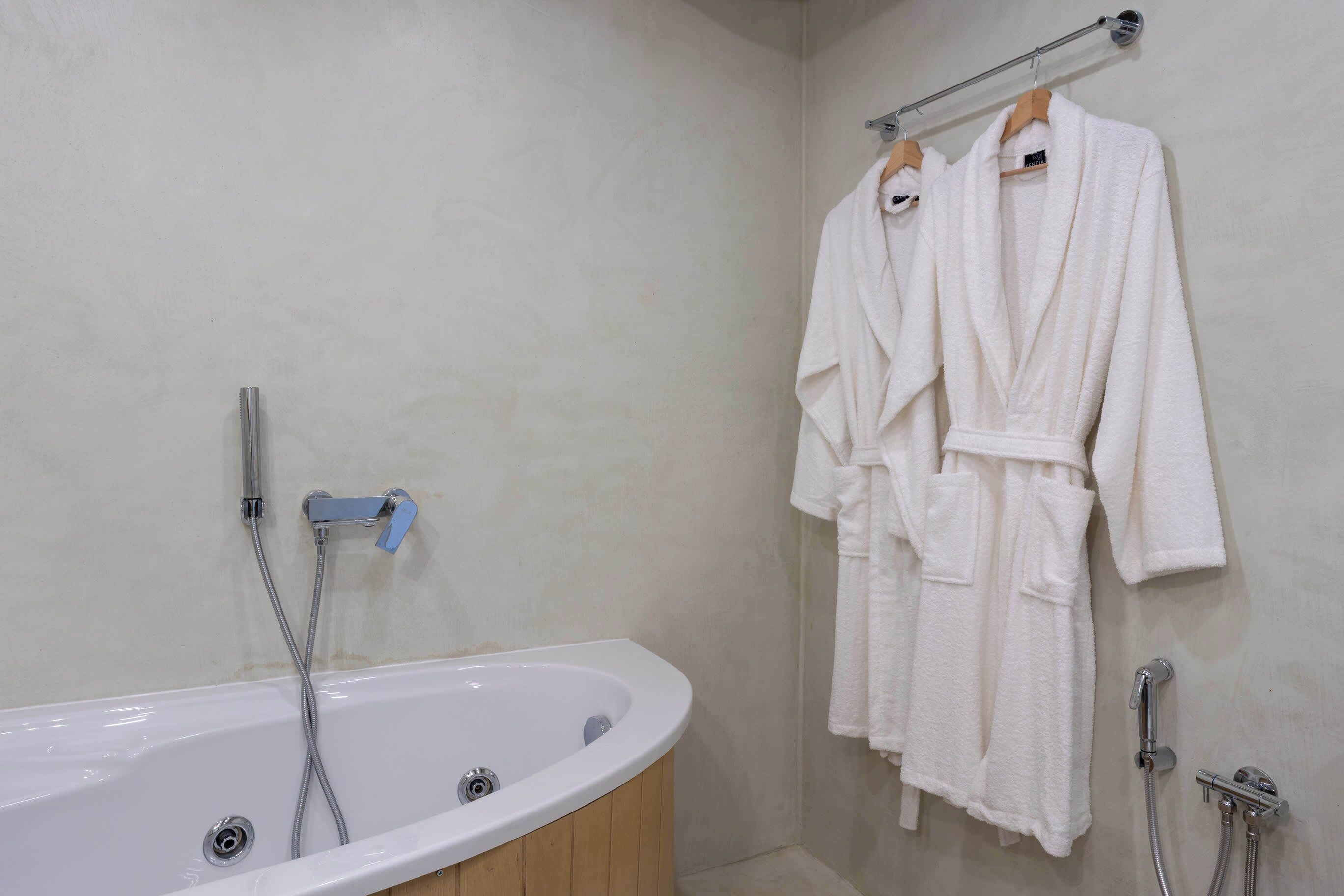 A bathroom with a bathtub, a shower, and two white robes hanging on a rack.