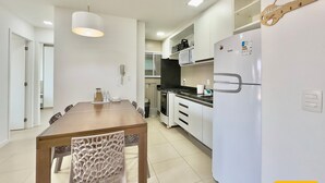 Una cocina moderna con armarios blancos, encimera negra y refrigerador blanco. En la pared, un cartel de bienvenida con forma de guitarra de madera.