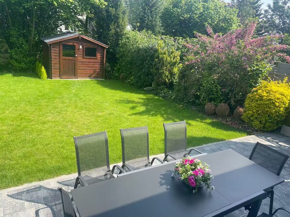 Une terrasse avec une table et des chaises, un vase de fleurs et un abri de jardin en bois.