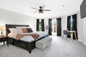 Ein Schlafzimmer mit Bett, Nachttisch, Bank, Deckenventilator und Schreibtisch mit Stuhl.