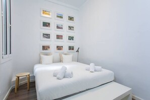 A hotel room with a large bed, a small wooden stool, and a wall with framed pictures. - Modern Flat, Amazing Terrace / Paseo de Gracia (08007 Barcelona)