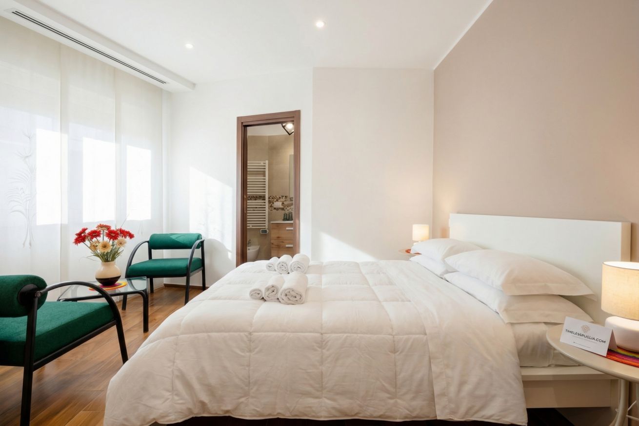 A hotel room with a bed, a chair, a nightstand, a lamp, and a view of a bathroom.