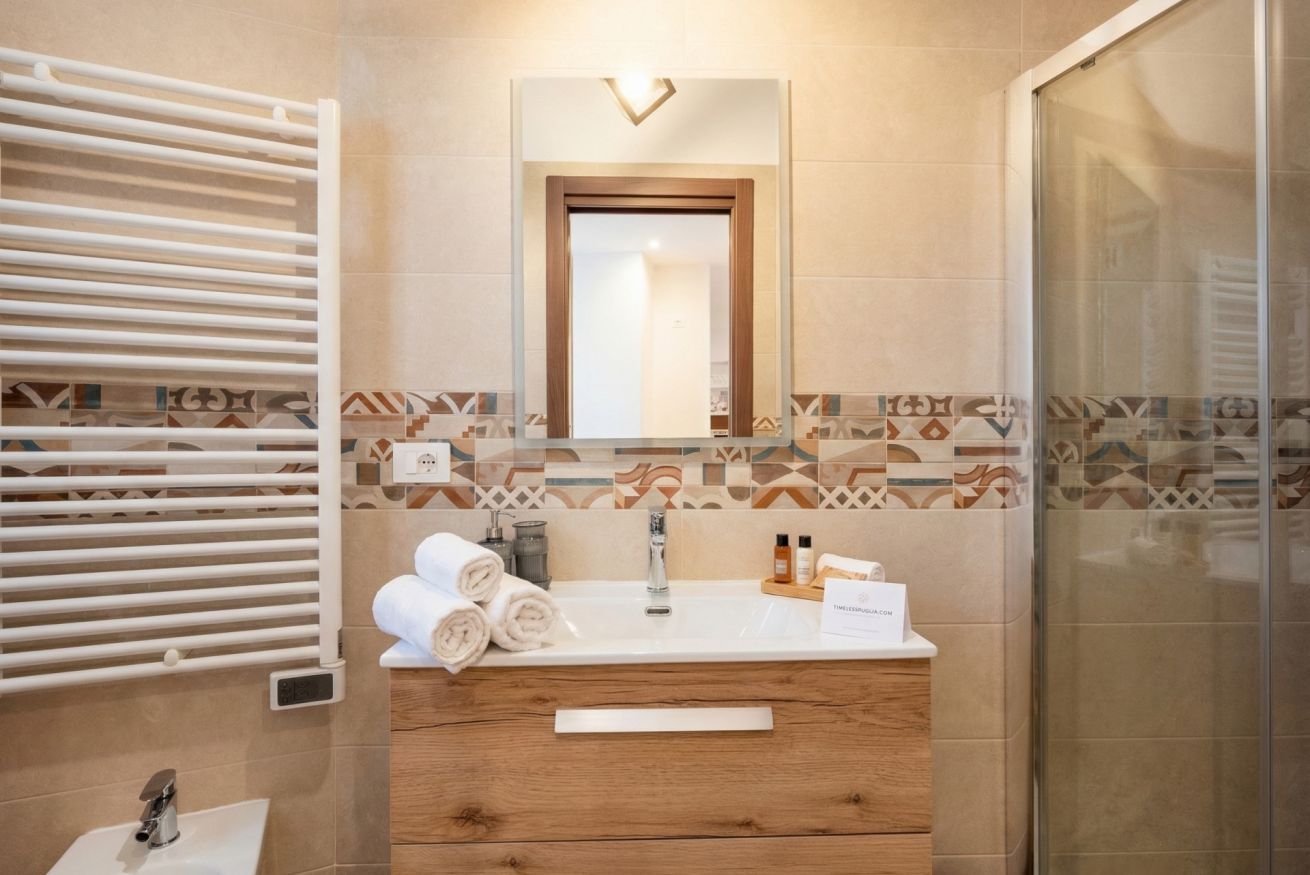 Een badkamer met een witte wastafel, houten opbergmeubel, handdoekrek en betegelde vloer.