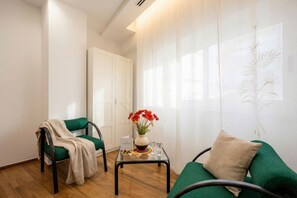A room with a green sofa, a chair with a blanket, a small table with a vase of flowers, and a white door. - Bengasi Central Loft – Stile, Comfort e Serenità (Bari)