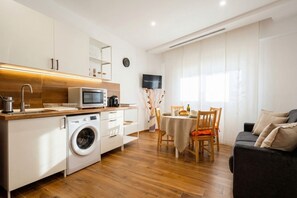 A compact kitchen with a washing machine, microwave, and sink; a dining area with a table and chairs; a sofa; and a TV mounted on the wall. - Benghazi Central Loft - Style, Comfort and Serenity (Bari)