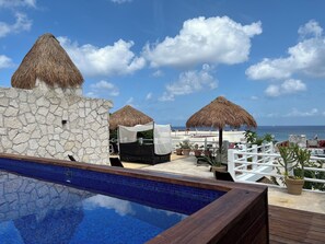 A pool area with a stone wall, a thatched umbrella, and a view of the ocean.