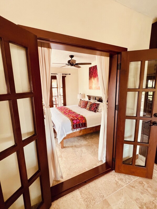 A bedroom with a bed, a ceiling fan, and a view through a glass door.