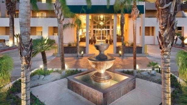 A hotel entrance with a central fountain, palm trees, and a well-lit building facade. - Palm Springs | Relaxing Desert Escape | Pool + Hot Tub (Palm Springs)