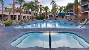 A swimming pool with lounge chairs and umbrellas, surrounded by palm trees and a building with balconies. - Palm Springs | Relaxing Desert Escape | Pool + Hot Tub (Palm Springs)