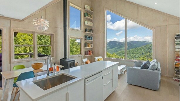 A modern kitchen with a large island, built-in bookshelves, and a view of a mountainous landscape.