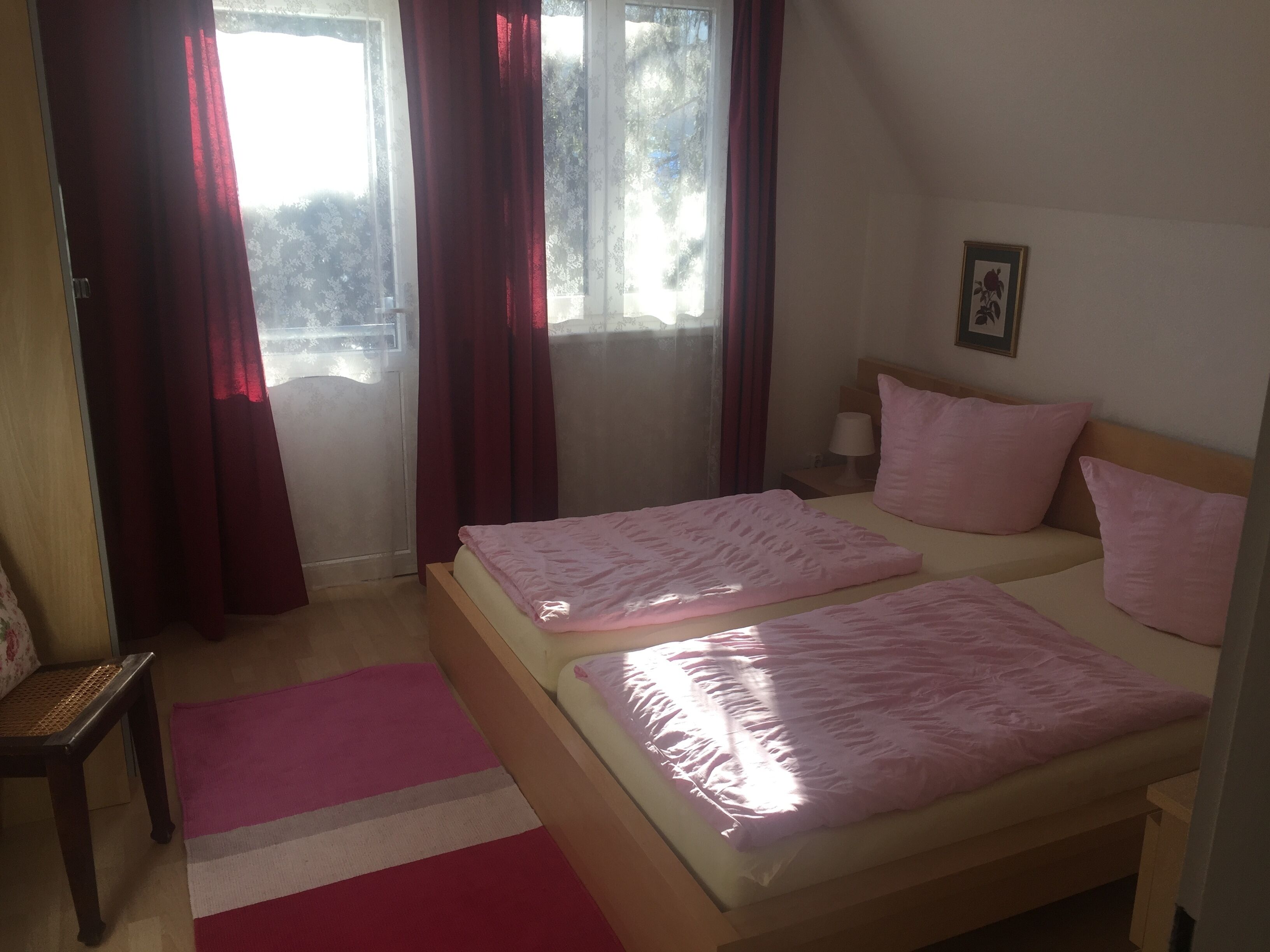 A bedroom with two beds, a wooden headboard, a bedside table with a lamp, and a window with curtains.