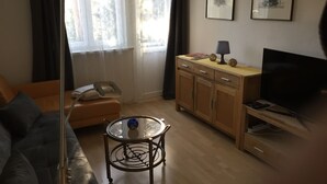 Uma sala de estar com sofá, mesa de vidro, armário de madeira e televisão.