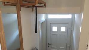 Uma escadaria com corrimão de madeira, uma porta branca com uma pequena janela e um porta-roupas fixado na parede.