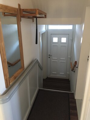 A staircase with a wooden handrail, a white door with a small window, and a wall-mounted coat rack. - Cozy vacation apartment with dream view and balcony on the hill in Wernigerode (Wernigerode)