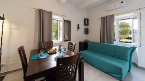 A dining area with a table set for two, a teal sofa, and a window with curtains. - Casa Ulisse with large garden and parking (Campo nell'Elba)