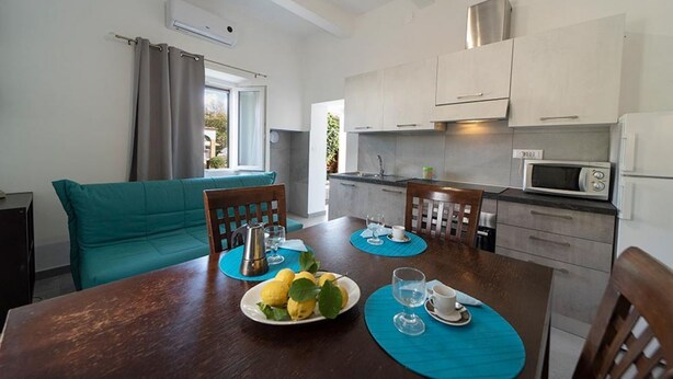 A compact kitchen with modern appliances, a dining area with a table set for two, and a teal sofa. - Casa Ulisse with large garden and parking (Campo nell'Elba)