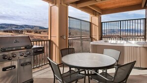 A covered outdoor patio with a grill, round table, and chairs, overlooking a mountainous landscape.