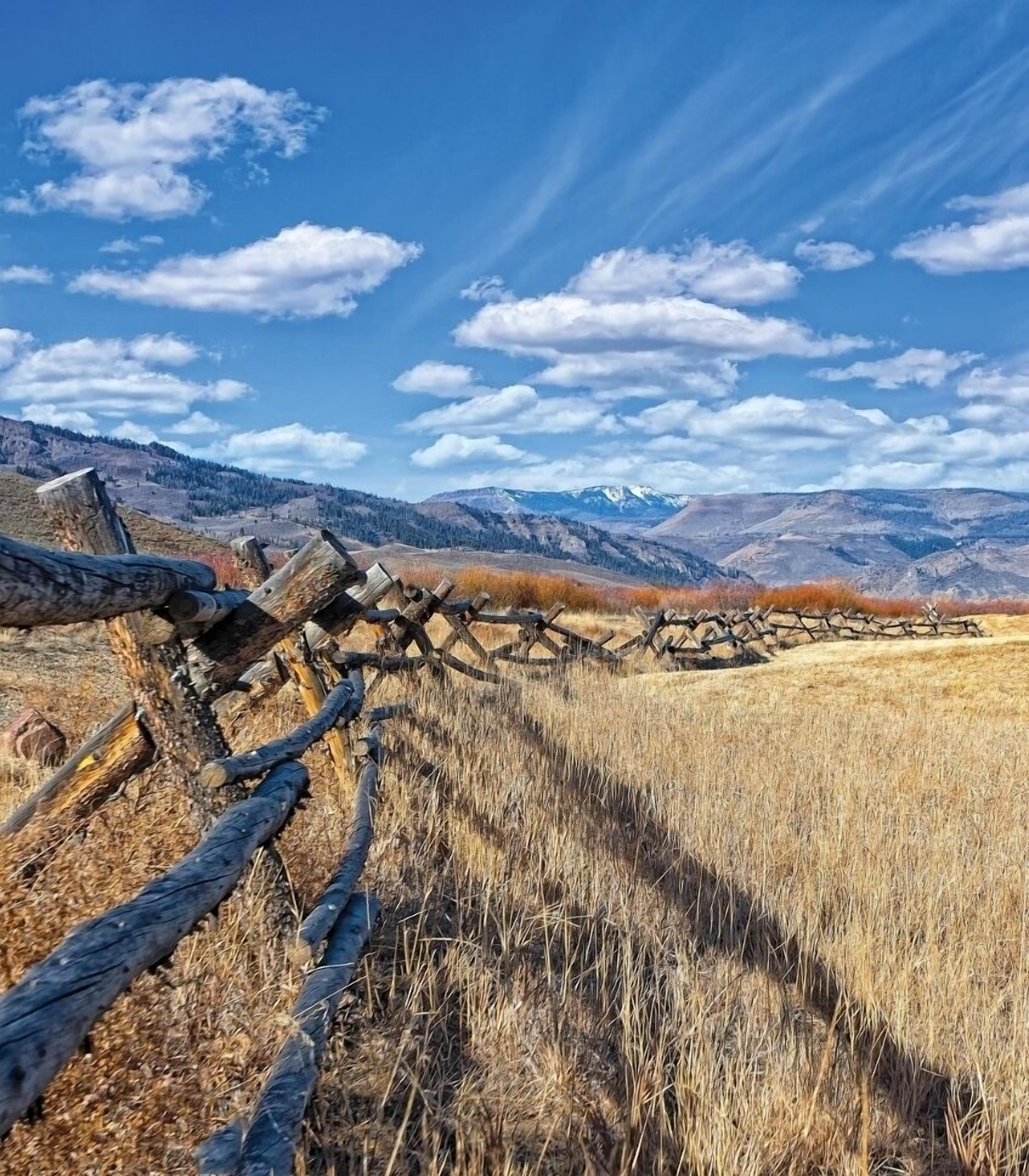 A rustic wooden fence in a dry field with mountains in the background.