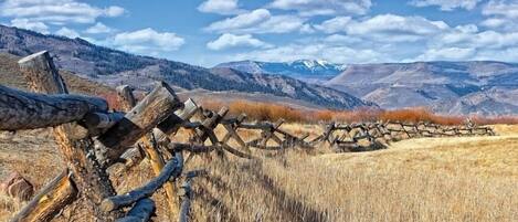 A rustic wooden fence in a dry field with mountains in the background.
