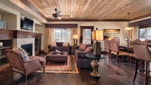 A spacious living room with a fireplace, a ceiling fan, and a dining area with patterned chairs.