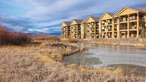 A multi-story hotel with balconies, a river in front, and a mountainous backdrop.