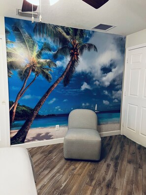 A room with a beach mural, a grey armchair, wooden flooring, and a white door. - Melbourne Serenity Retreat! (Melbourne)