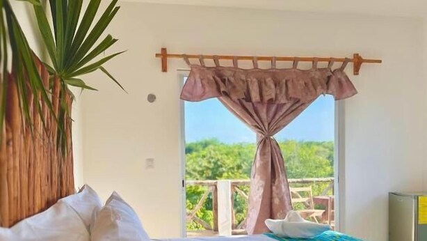 A bedroom with a bed, a view of greenery outside, and a plant on the left. - Hotel Ich Ha Tulum - Adults Only  (Tulum)