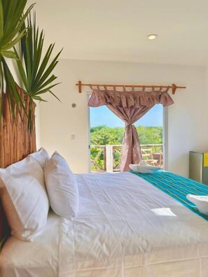 A bedroom with a bed, a view of greenery outside, and a plant on the left. - Hotel Ich Ha Tulum - Adults Only  (Tulum)