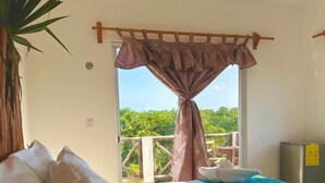 A bedroom with a bed, a window with curtains, a plant, and a balcony with a railing. - Hotel Ich Ha Tulum - Adults Only  (Tulum)