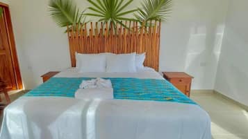 Una habitación de hotel con una cama, un cabecero de madera, una colcha azul y blanca estampada, y dos palmeras sobre el cabecero.