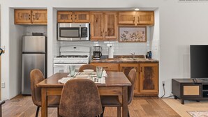 Une cuisine compacte dotée de meubles en bois, d’un four à micro-ondes, d’une cuisinière, d’un réfrigérateur et d’une table à manger avec des chaises.