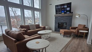 A spacious living room with a fireplace, large windows, and a balcony.